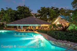 Relax by the pool surrounded by lush greenery and a thatched-roof bar.