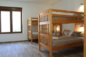 Een kamer met twee stapelbedden, een raam en een nachtkastje met een lamp.