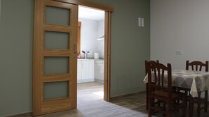 Une pièce dotée d’une porte en bois donnant sur une cuisine, d’une table à manger avec des chaises et d’un plancher de couleur claire.