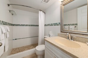 A modern bathroom with a shower, toilet, sink, and a large mirror. - Location, location, location - 7 Mile Beach Oceanfront 3BR at Sunset Cove! (Grand Cayman SC302)