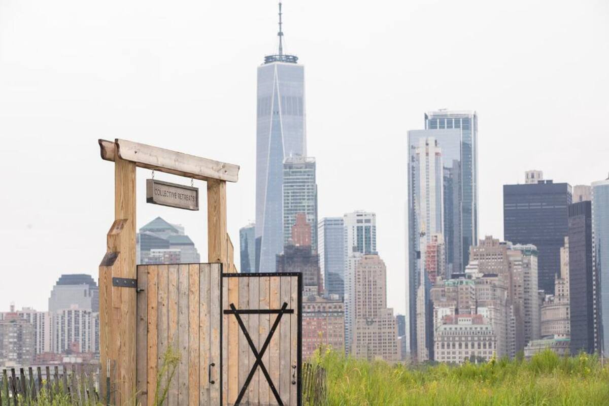 Una verja de madera con un letrero que dice "COLLECTIVE RETREATS" frente a un horizonte urbano.