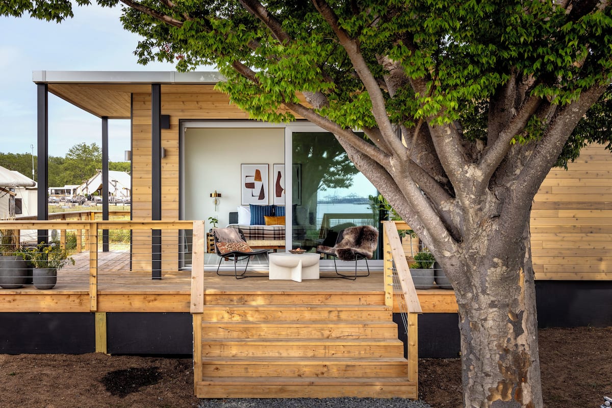 Una casa moderna con una terraza de madera, una escalera y un árbol grande en primer plano.
