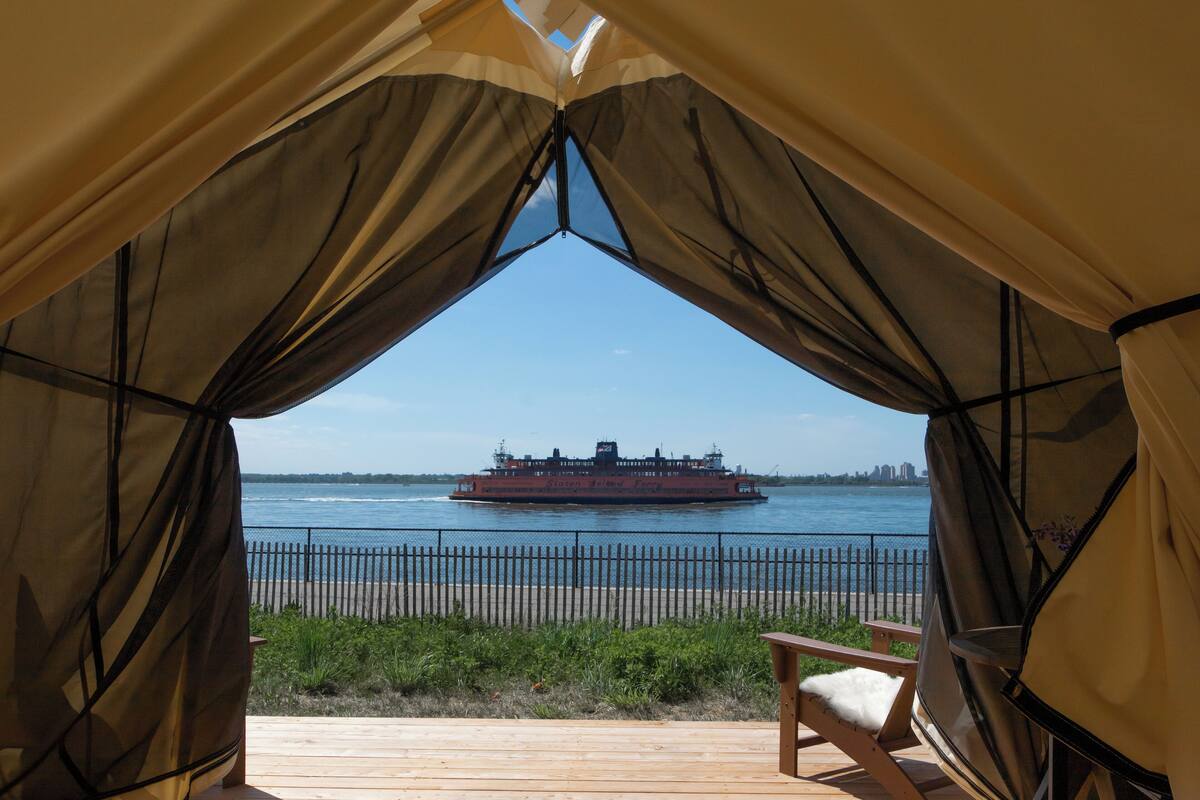 Vista desde una zona con carpas, que da al río, con una embarcación grande, una terraza de madera y una silla.
