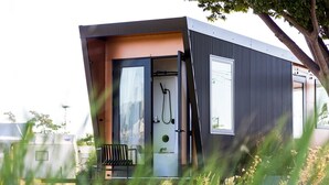 A modern, compact cabin with a sliding door, a small seating area, and a visible shower. - Collective Retreats Governors Island (New York)