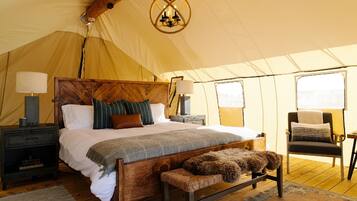 A tented room with a wooden bed, two bedside tables, a bench, and a chair.