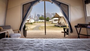 A tent with a city view, a bed, a chair, a table, and a plant. - Collective Retreats Governors Island (New York)