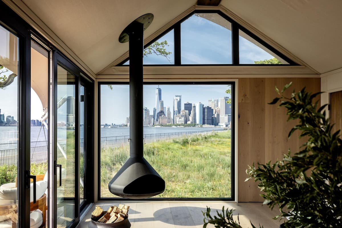 Un interior moderno con amplios ventanales que ofrecen vista al horizonte de la ciudad, una lámpara colgante negra y piso de madera.