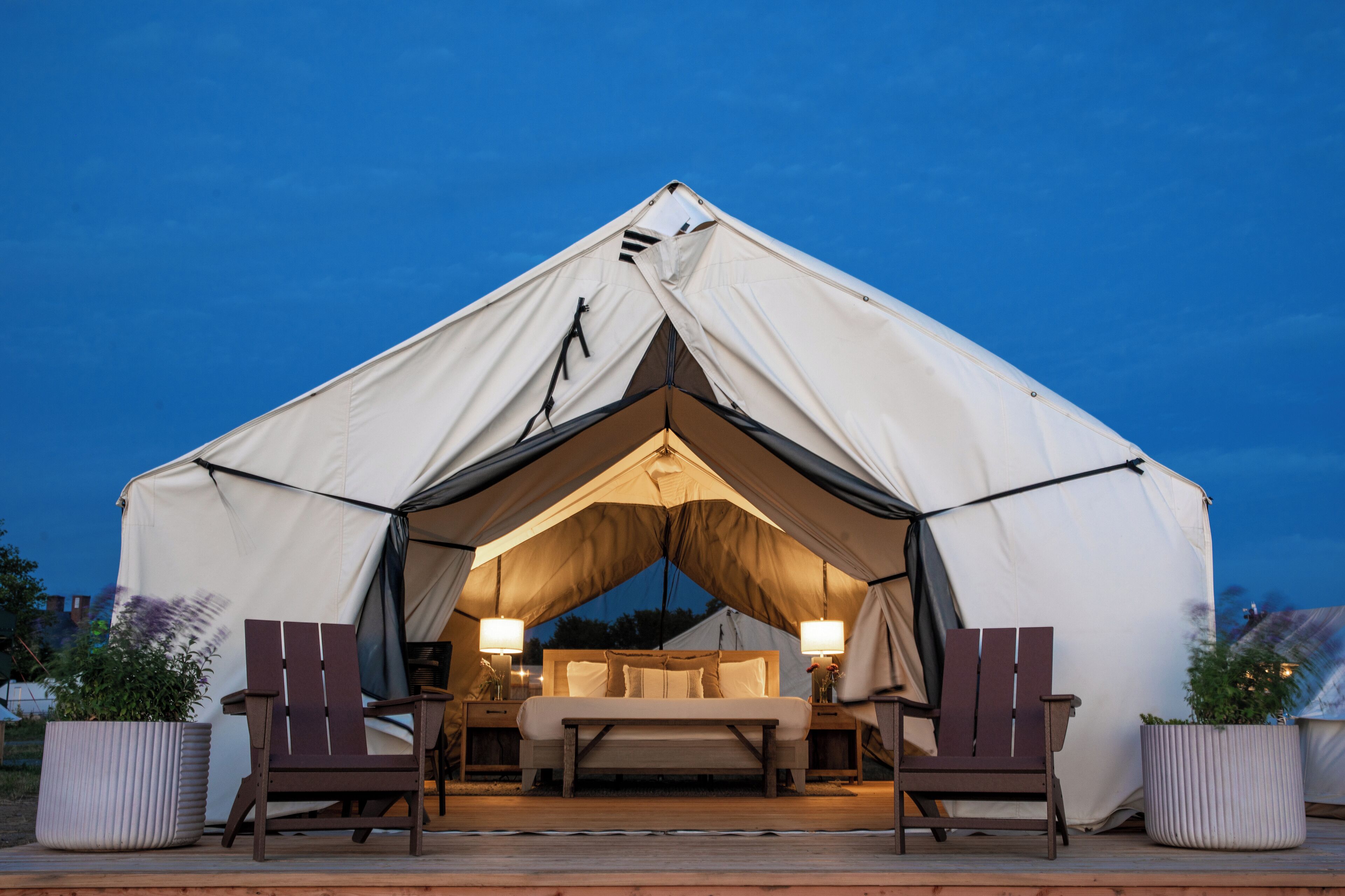 A tent with a bed, two chairs, and two bedside tables with lamps.
