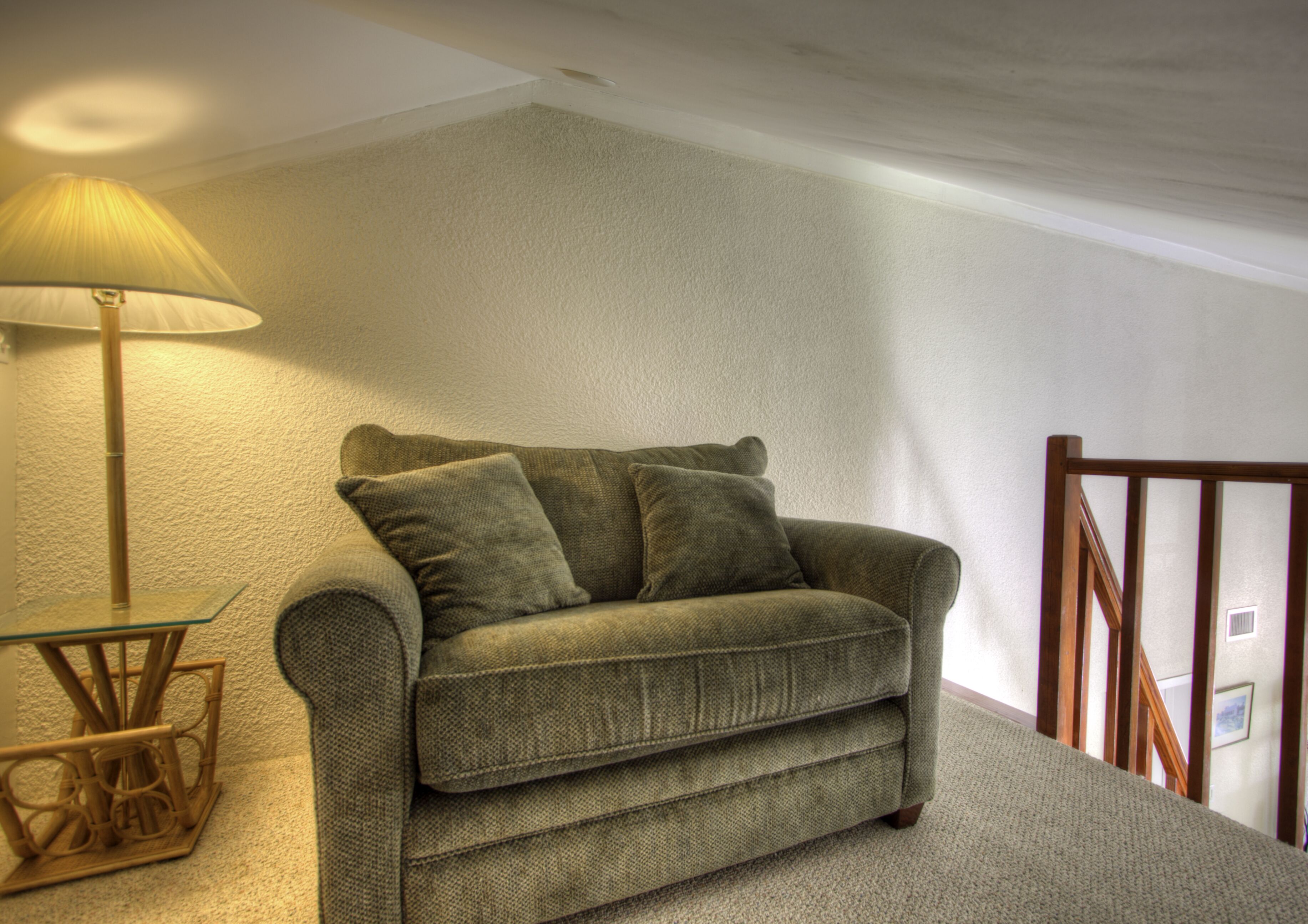 Une pièce d’angle avec un canapé vert, une lampe et une chaise en bois.
