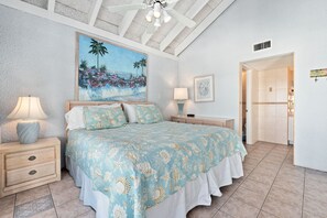 A bedroom with a bed, nightstands, a painting, and a door leading to another room.