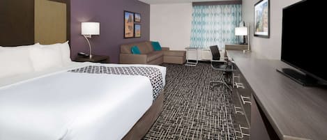 Una habitación de hotel con una cama grande, un escritorio con una silla, un televisor y una pequeña zona de estar con un sofá y una mesa.