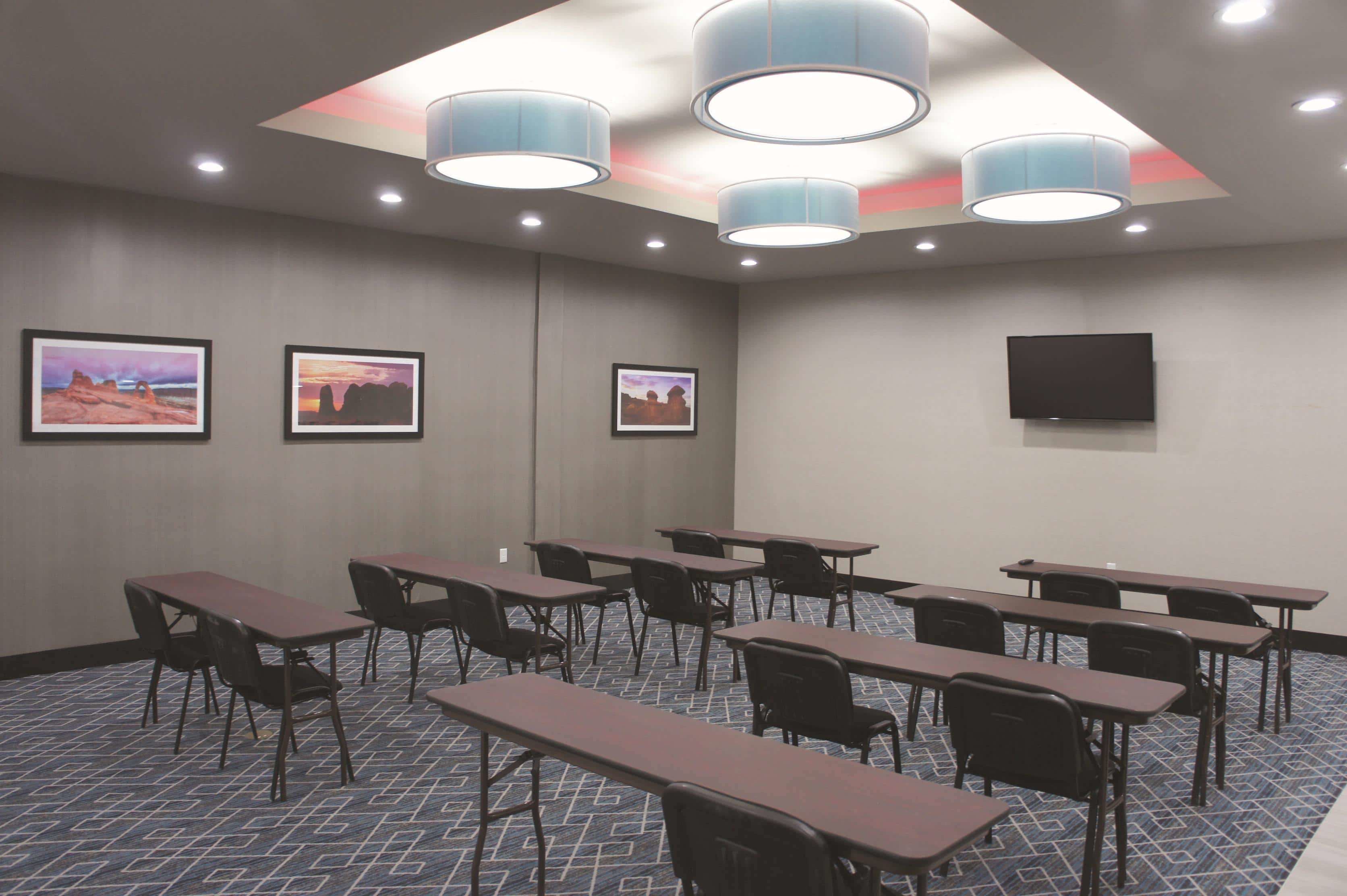 A conference room with tables and chairs, ceiling lights, and framed pictures on the walls.