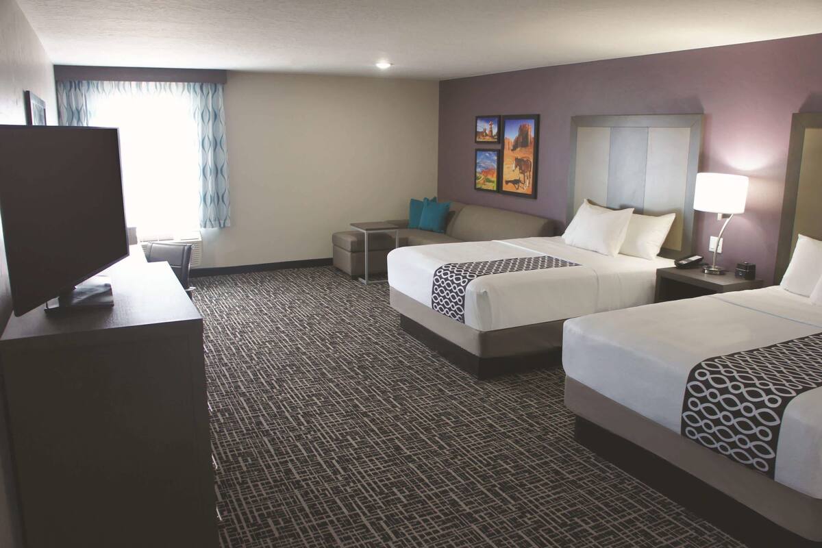 Una habitación de hotel con dos camas, un escritorio, un televisor y una ventana con cortinas.