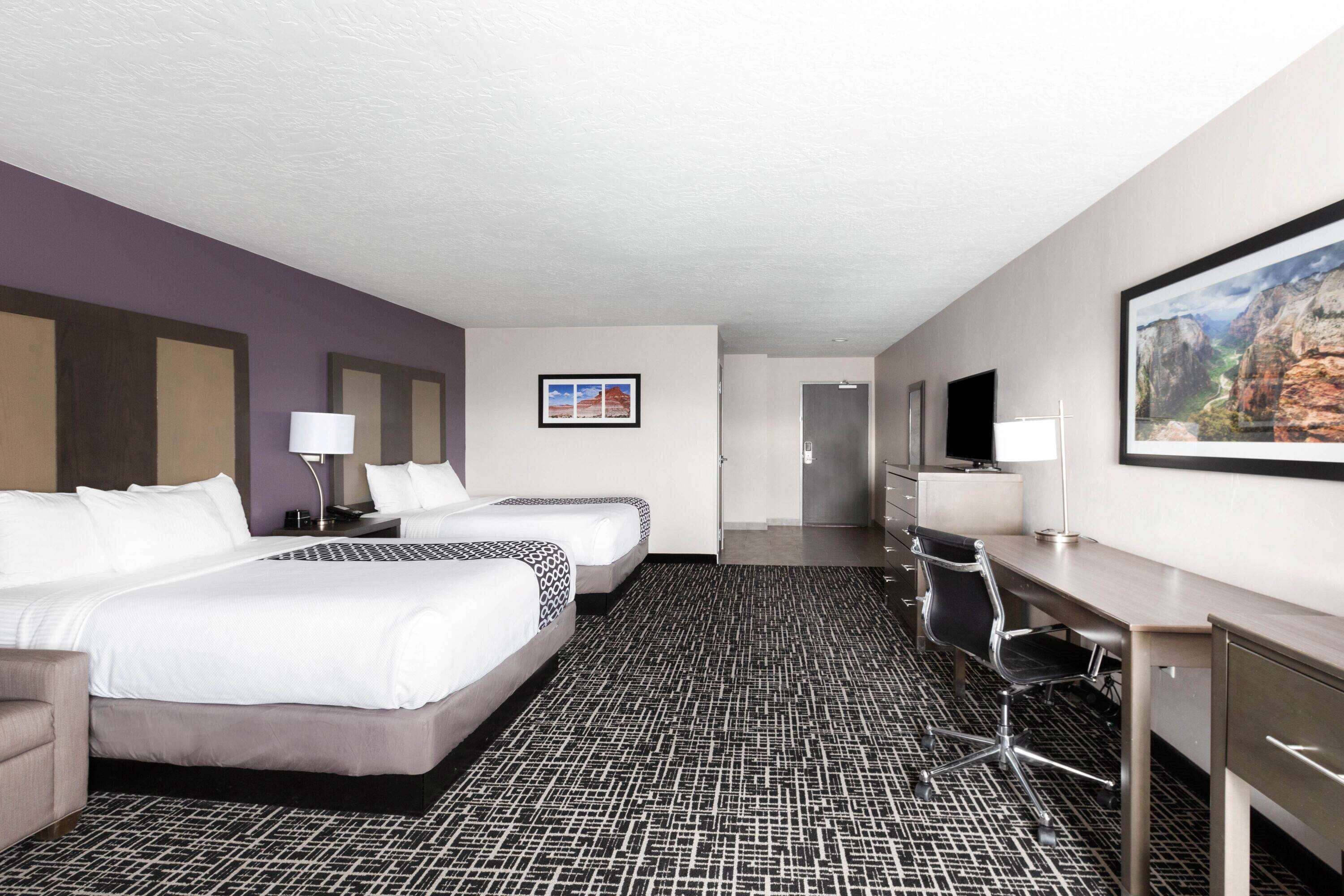 A hotel room with two beds, a desk, a chair, a TV, and a framed picture on the wall.