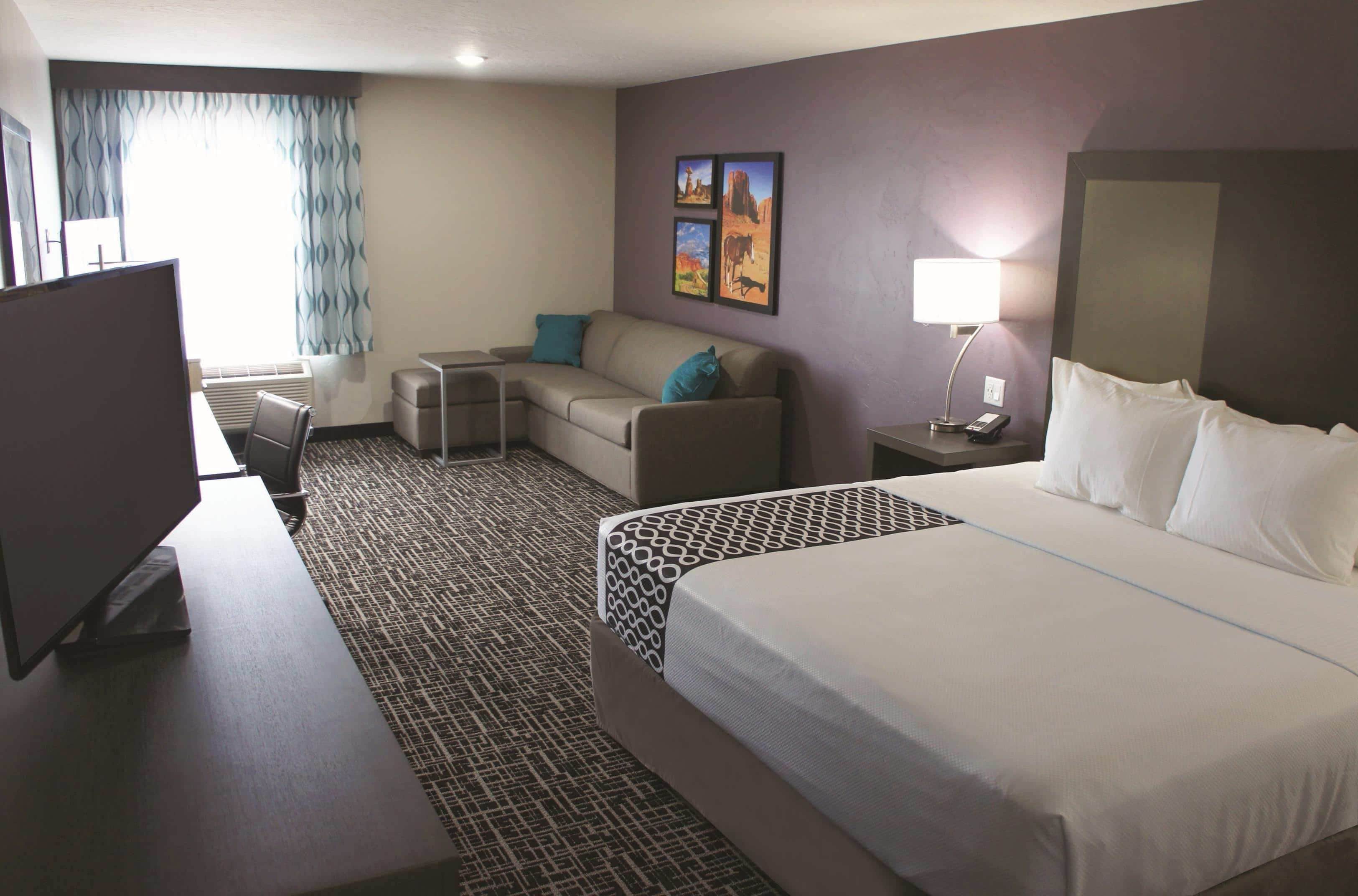 A hotel room with a large bed, a desk with a computer, a sofa, and a TV.