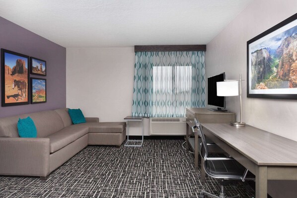 A hotel room with a sofa, a desk, a TV, and a window with patterned curtains.