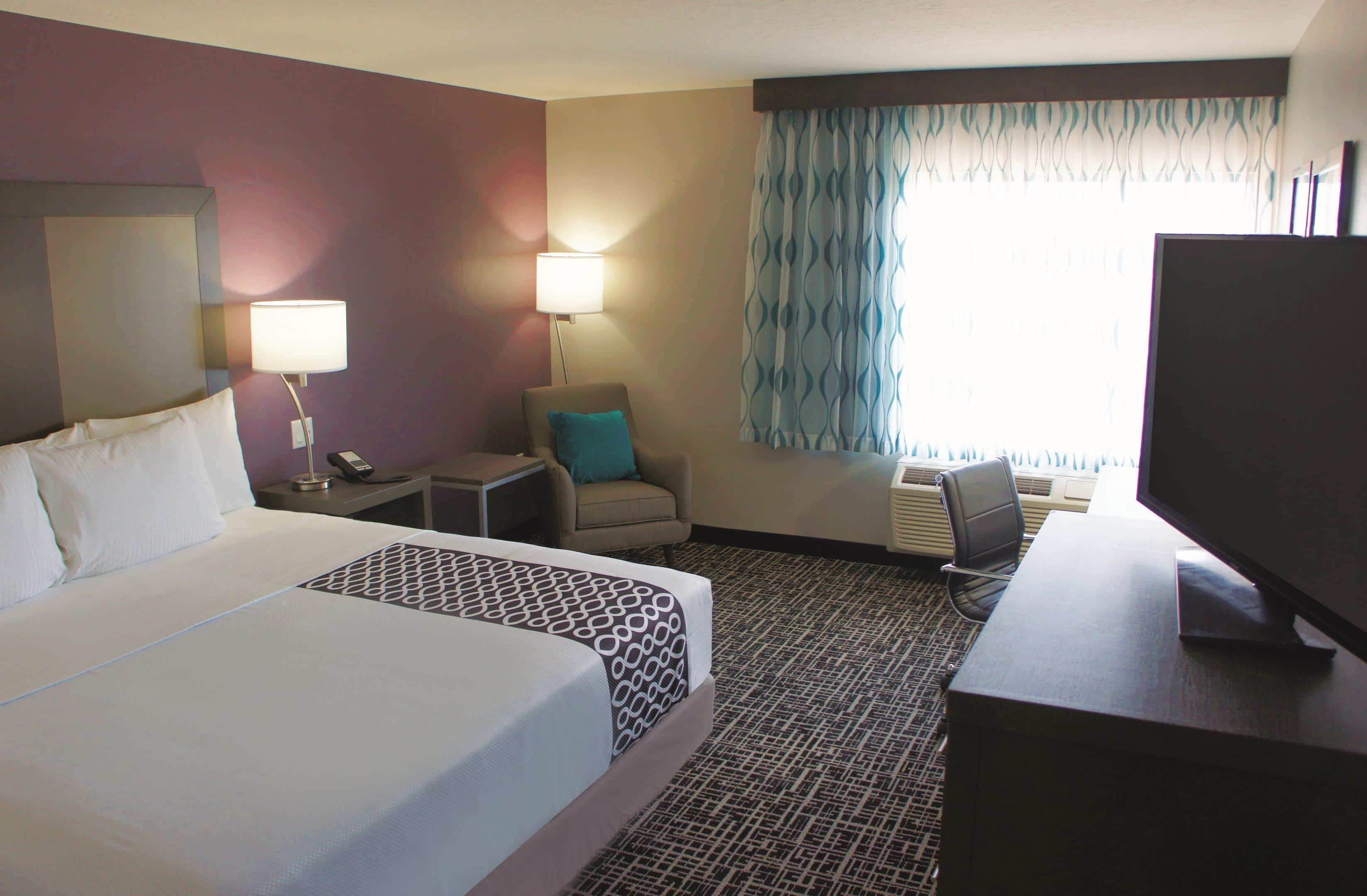A hotel room with a large bed, a desk with a computer, a chair, a lamp, and a TV.
