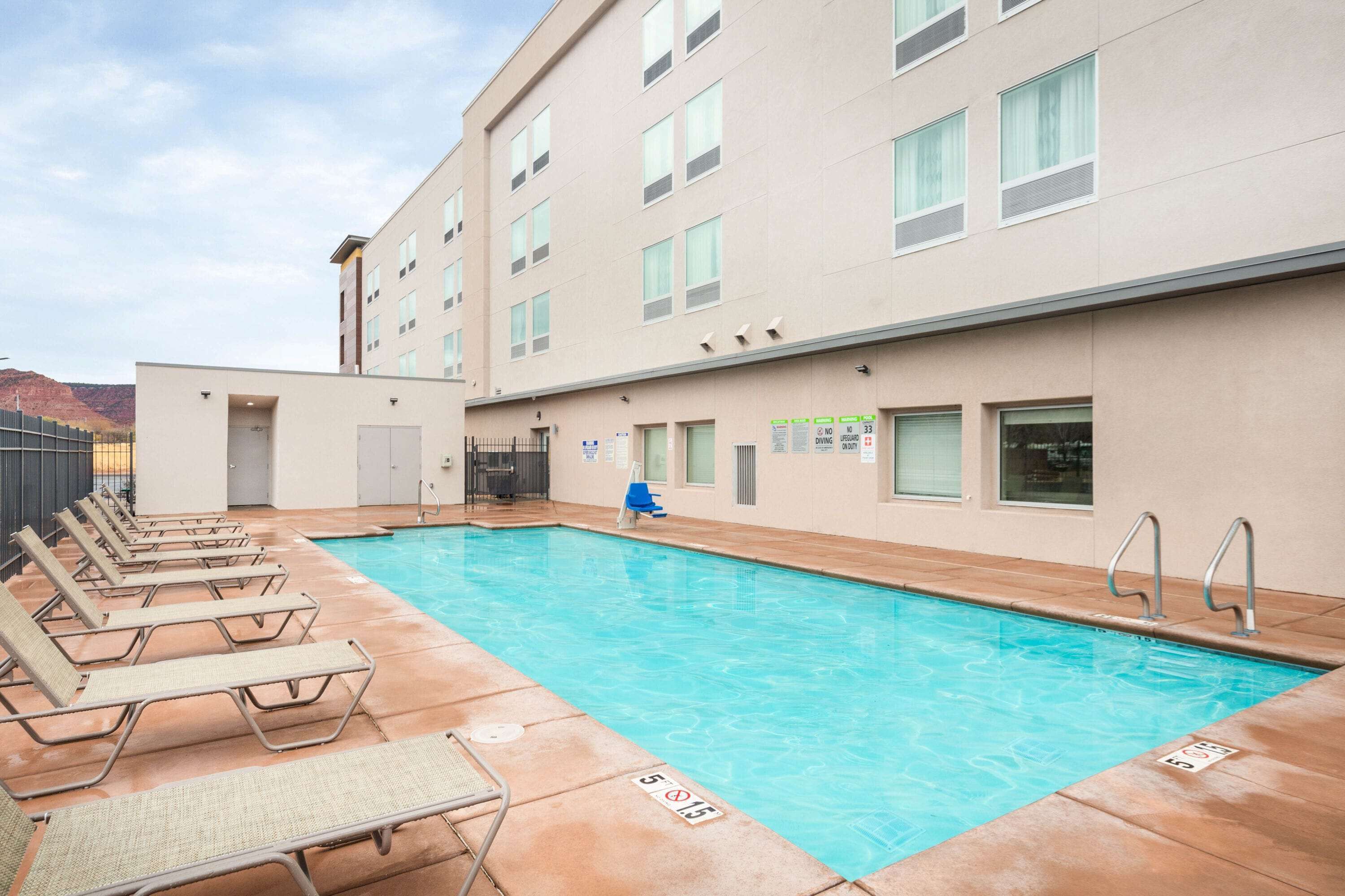 A pool area with lounge chairs and a building with multiple windows and signs.