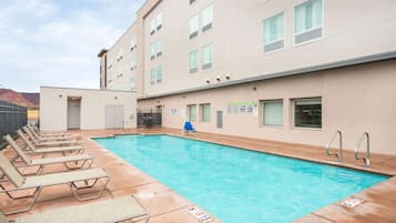 A pool area with lounge chairs and a building with multiple windows and signs.