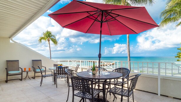 A terrace with a red umbrella, outdoor seating, and a view of the ocean.