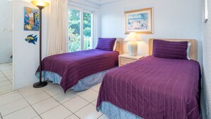 A room with two beds, a window with curtains, a lamp, and artwork on the walls.