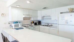 A modern kitchen with white cabinets, a microwave, stove, sink, and a refrigerator.