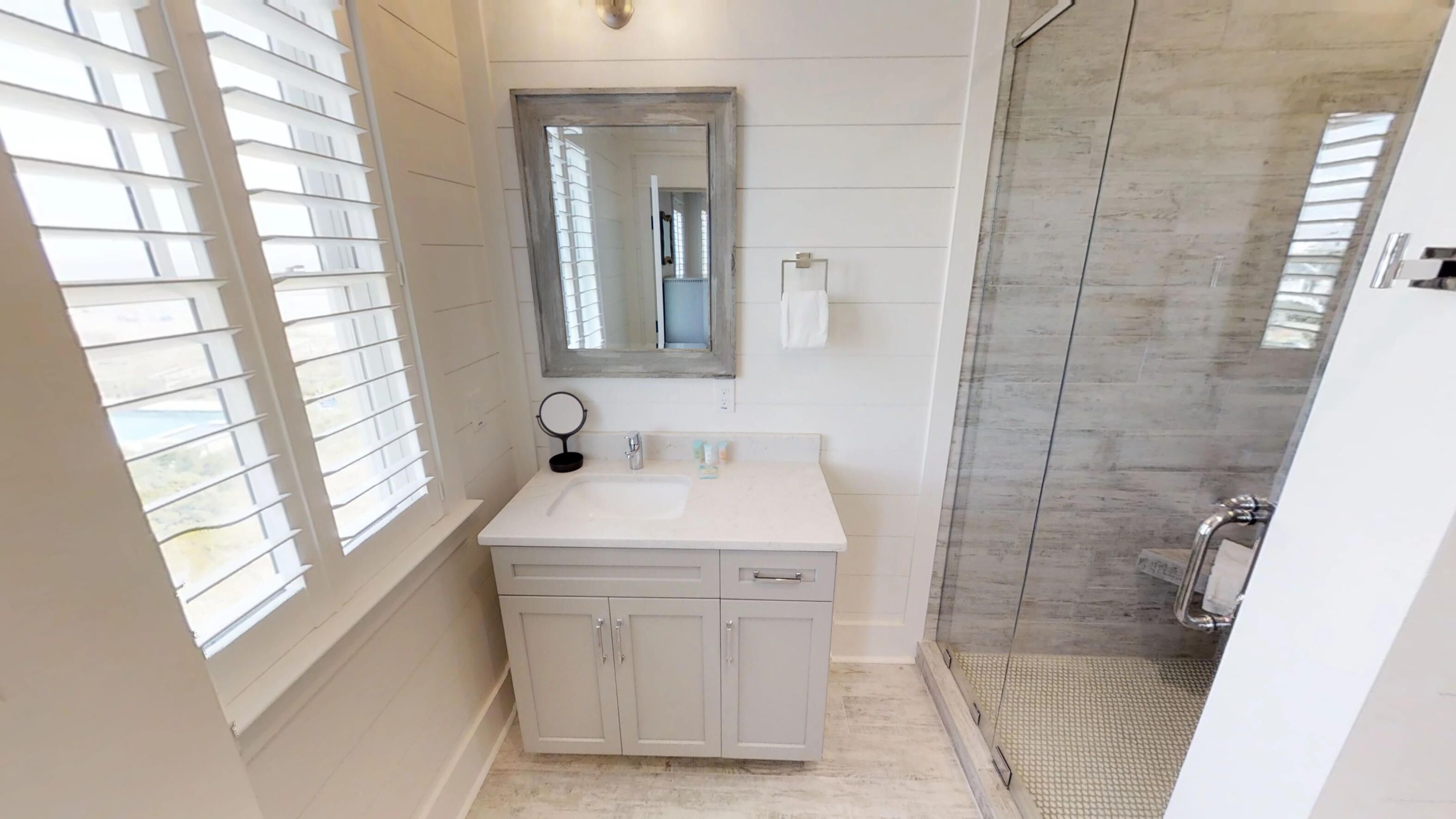 Une salle de bain avec un meuble-lavabo blanc, un miroir, un porte-serviettes et un espace douche.