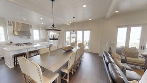 A spacious kitchen with a large island, a dining area with a long table and chairs, and a living area with a sofa and chairs.