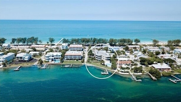 Vista aérea de un complejo turístico costero con varios edificios, un puerto deportivo y aguas azules cristalinas.