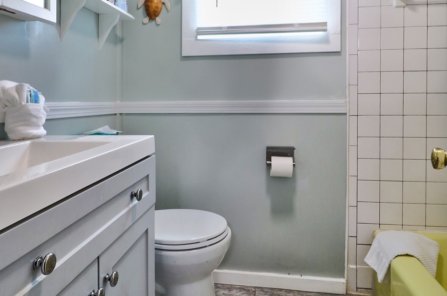 Un baño con inodoro blanco, lavamanos con toalla y un dispensador de papel higiénico en la pared.