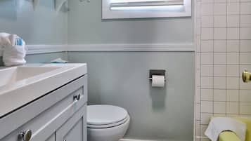 A bathroom with a white toilet, a sink with a towel, and a toilet paper holder on the wall.