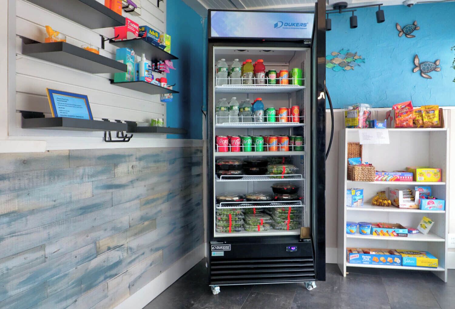 A vending machine stocked with beverages and snacks, shelves with various products, and a wall with a blue mural.