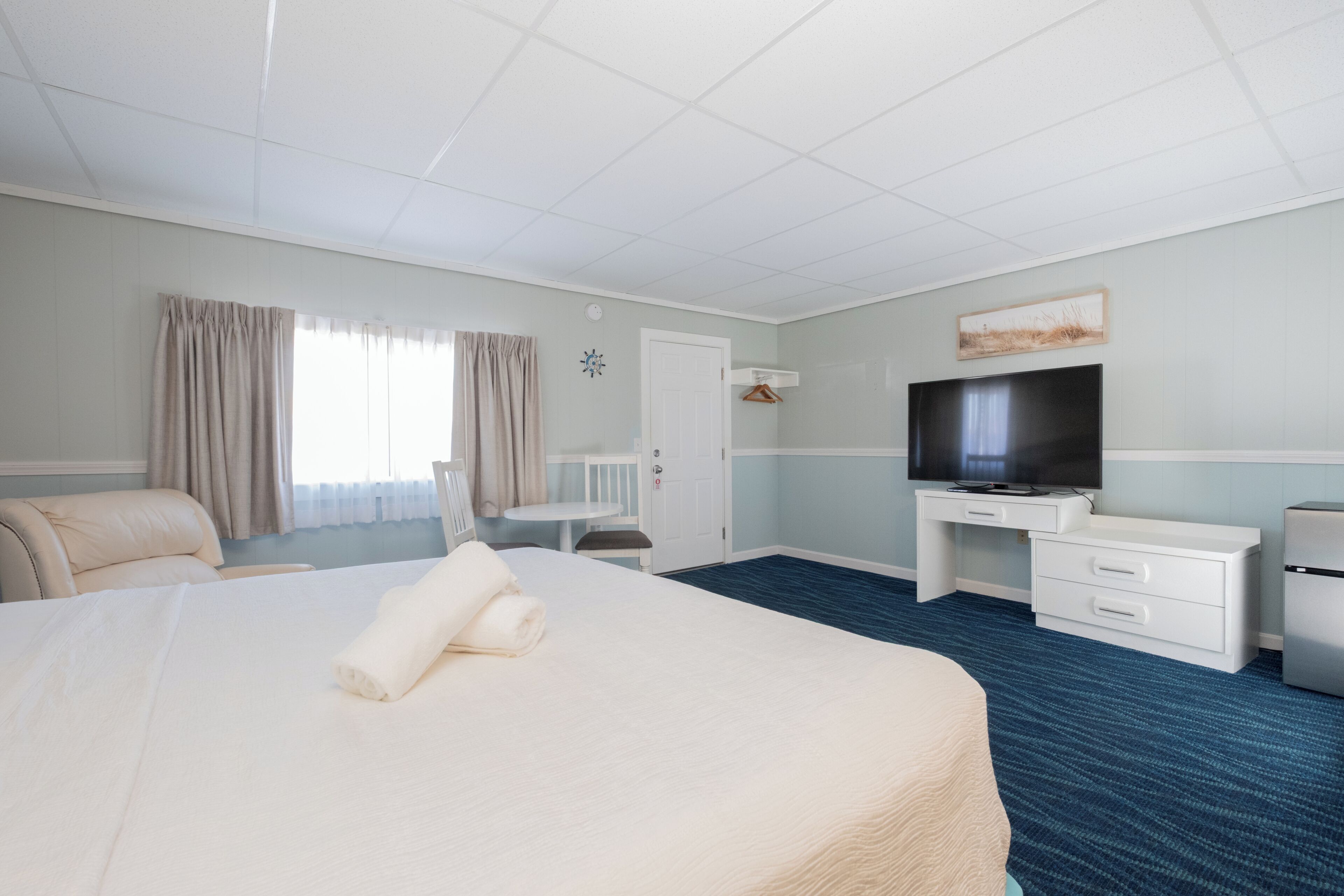 Una habitación de hotel con una cama grande, un escritorio con televisor, una silla y una mesita.
