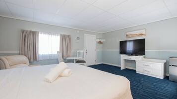 Ett hotellrum med en stor säng, ett skrivbord med en tv, en stol och ett litet bord.