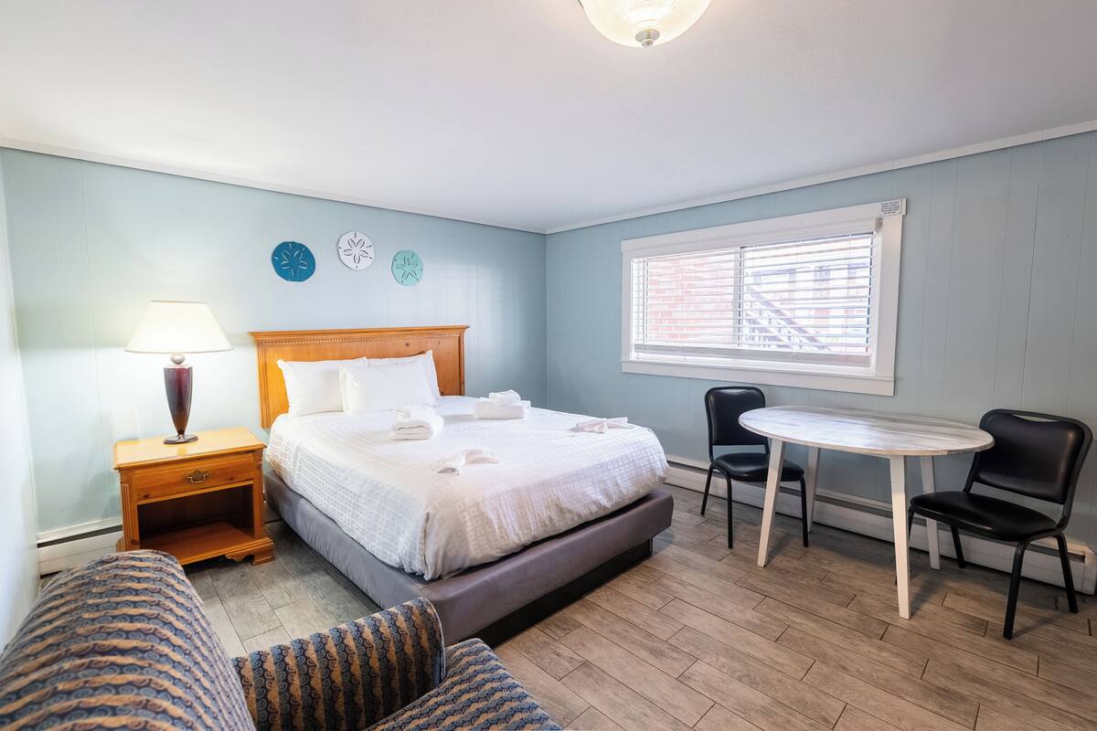 A bedroom with a bed, bedside table, lamp, and a small table with chairs.