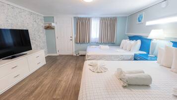 A hotel room with a flat-screen TV, a bed with white linens, a bedside table with a lamp, and a wooden floor.
