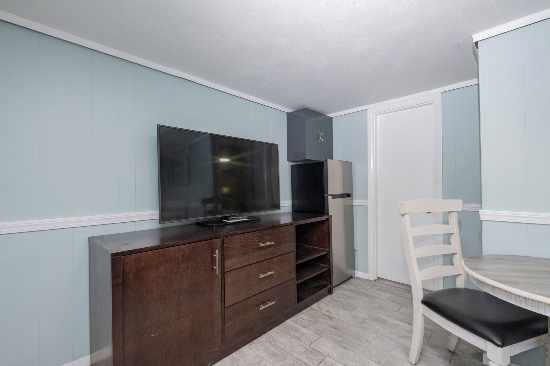Una habitación con un armario de madera oscura, un televisor de pantalla plana, una silla blanca y una puerta blanca.