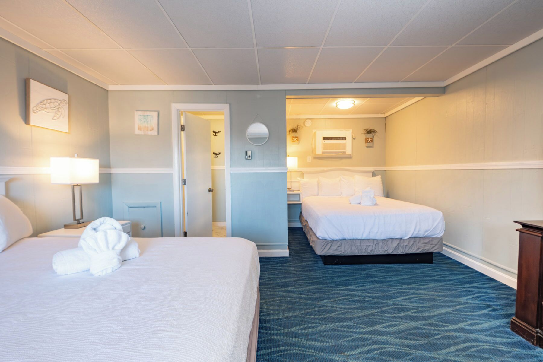 A hotel room with two beds, a bathroom, and a hallway.