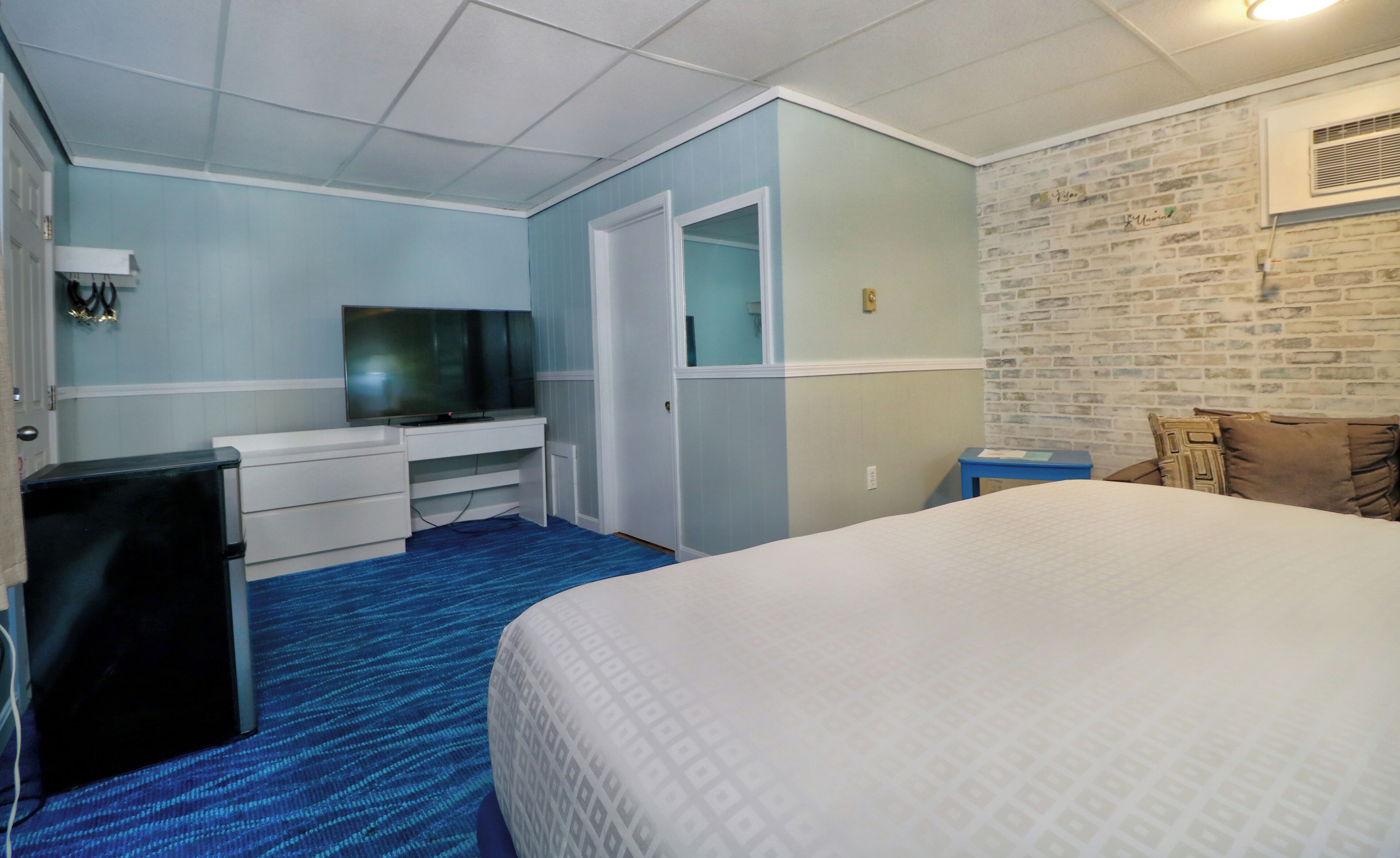 Habitación de hotel con una cama, un televisor en una cómoda blanca, un escritorio pequeño y una pared con diseño de ladrillo.