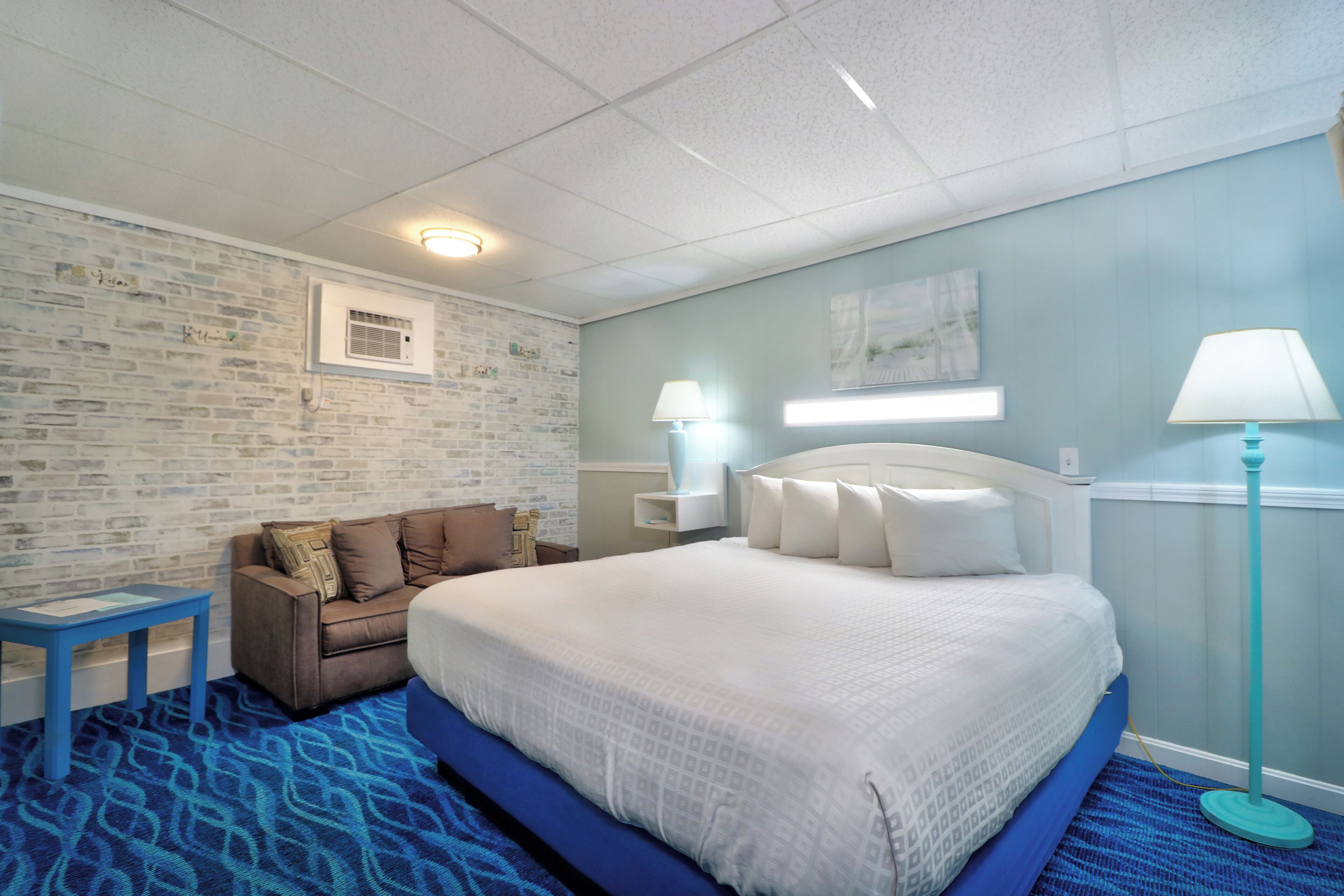 Habitación de hotel con una cama grande, un pequeño sofá, una mesita de noche y una lámpara.