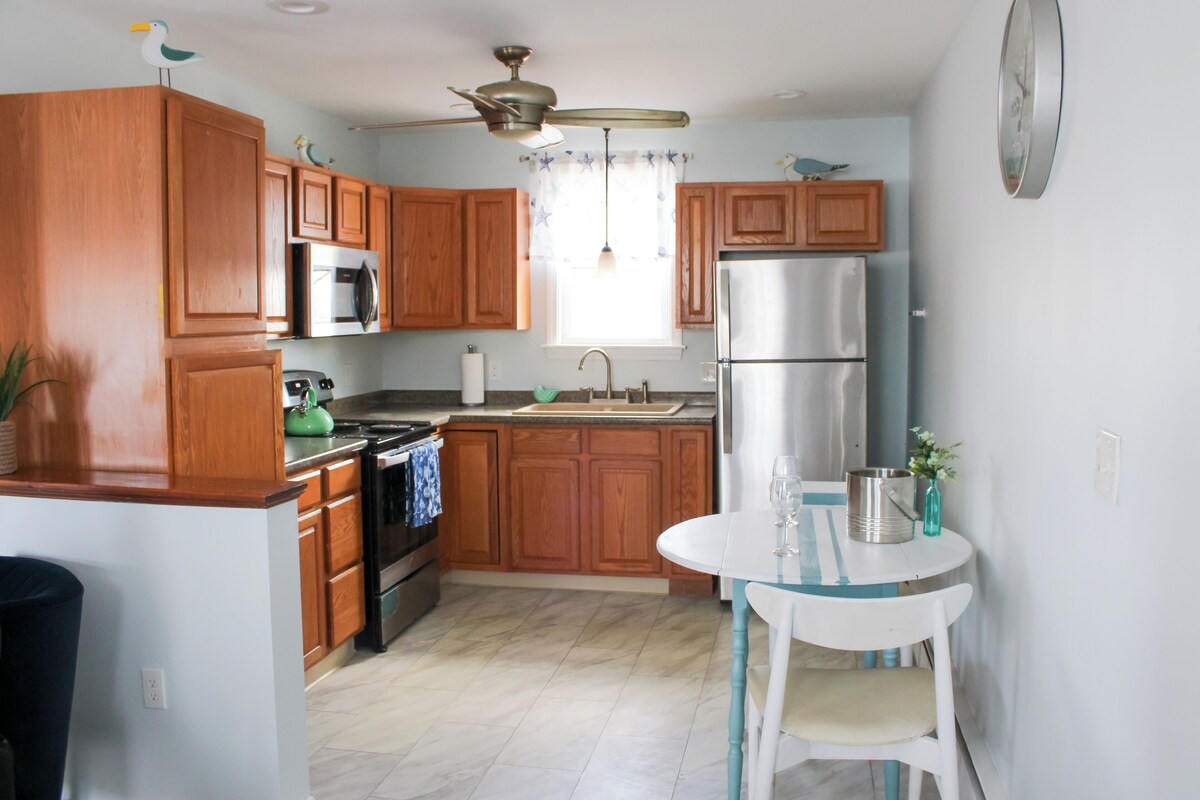 A kitchen with wooden cabinets, stainless steel appliances, a small dining table, and a ceiling fan.