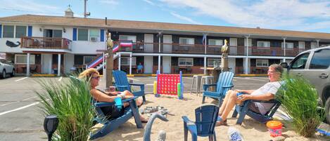 A motel with a pool area featuring lounge chairs, a children's play structure, and a statue of a mermaid.