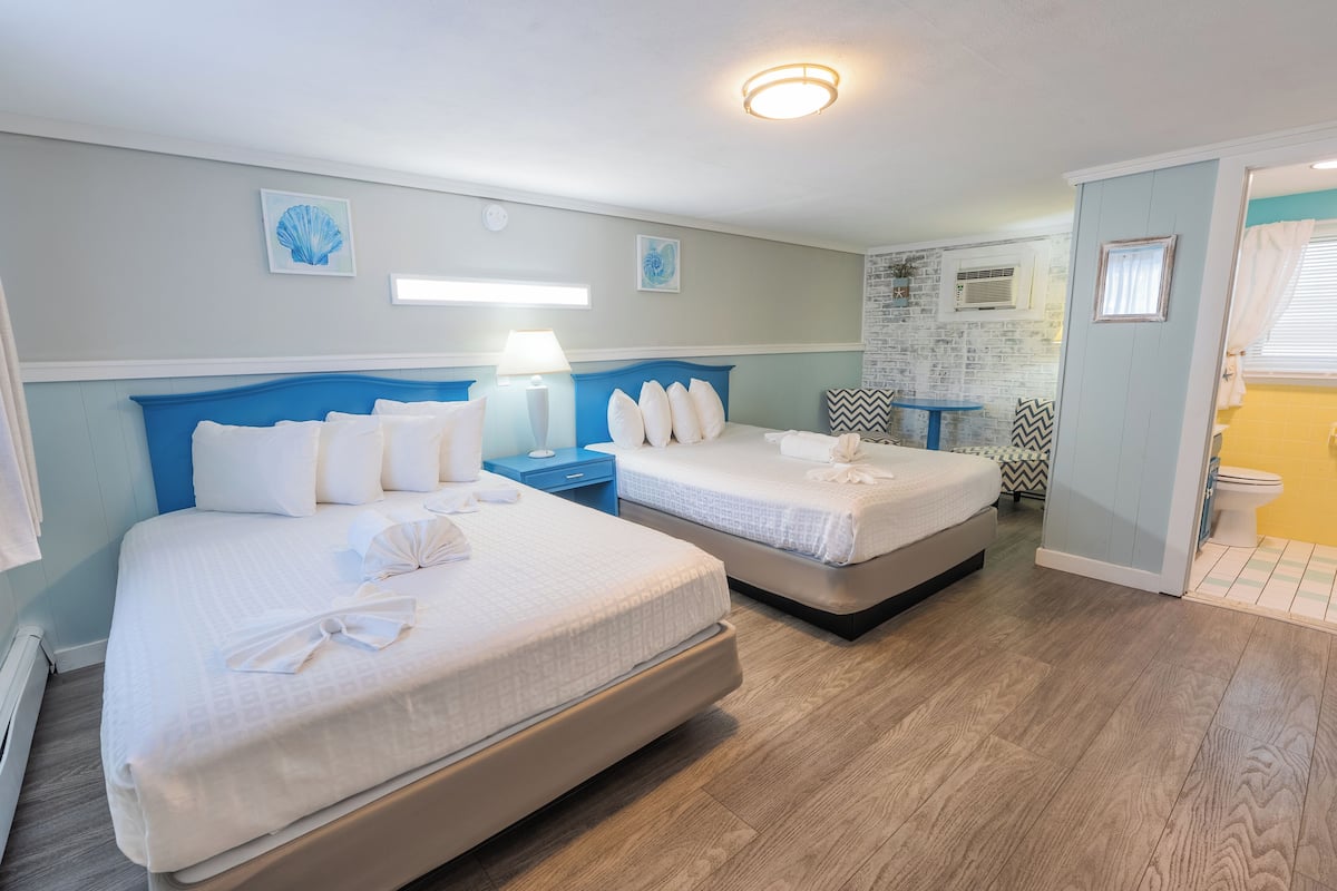 A hotel room with two beds, a nightstand, a lamp, and artwork on the walls.