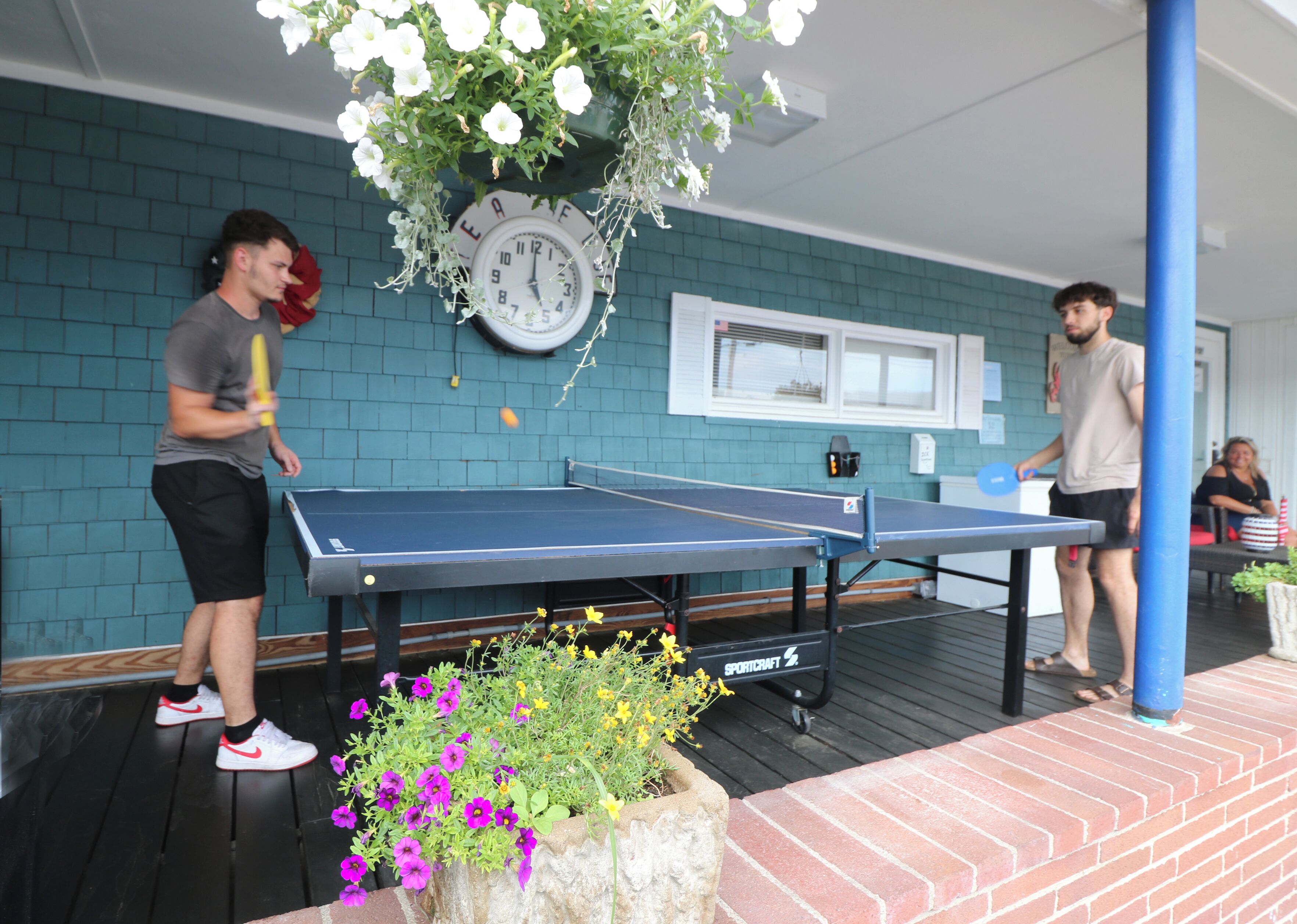 A ping pong table in a room with teal brick walls, a clock, and a flower planter.