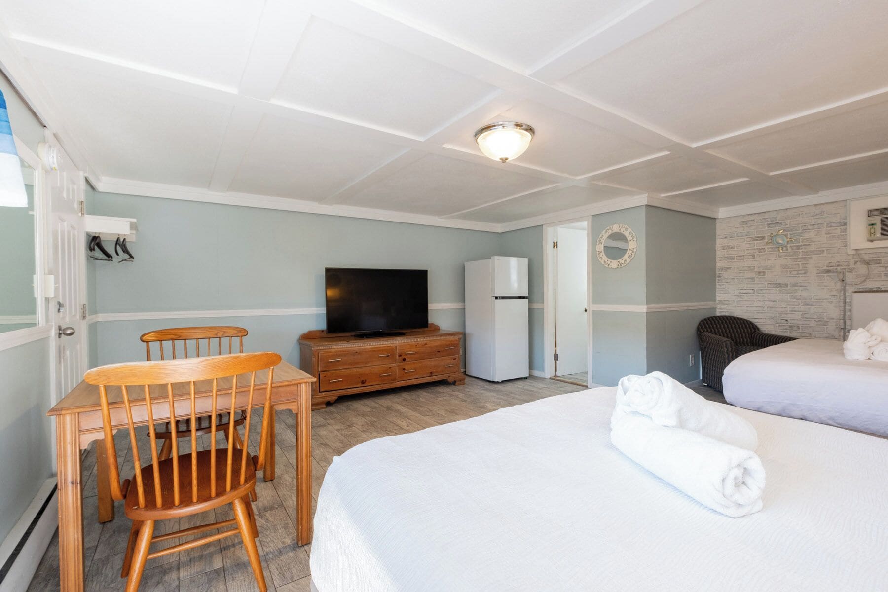Hotellihuone, jossa on sänky, televisio, lipasto, tuoli ja ovi.