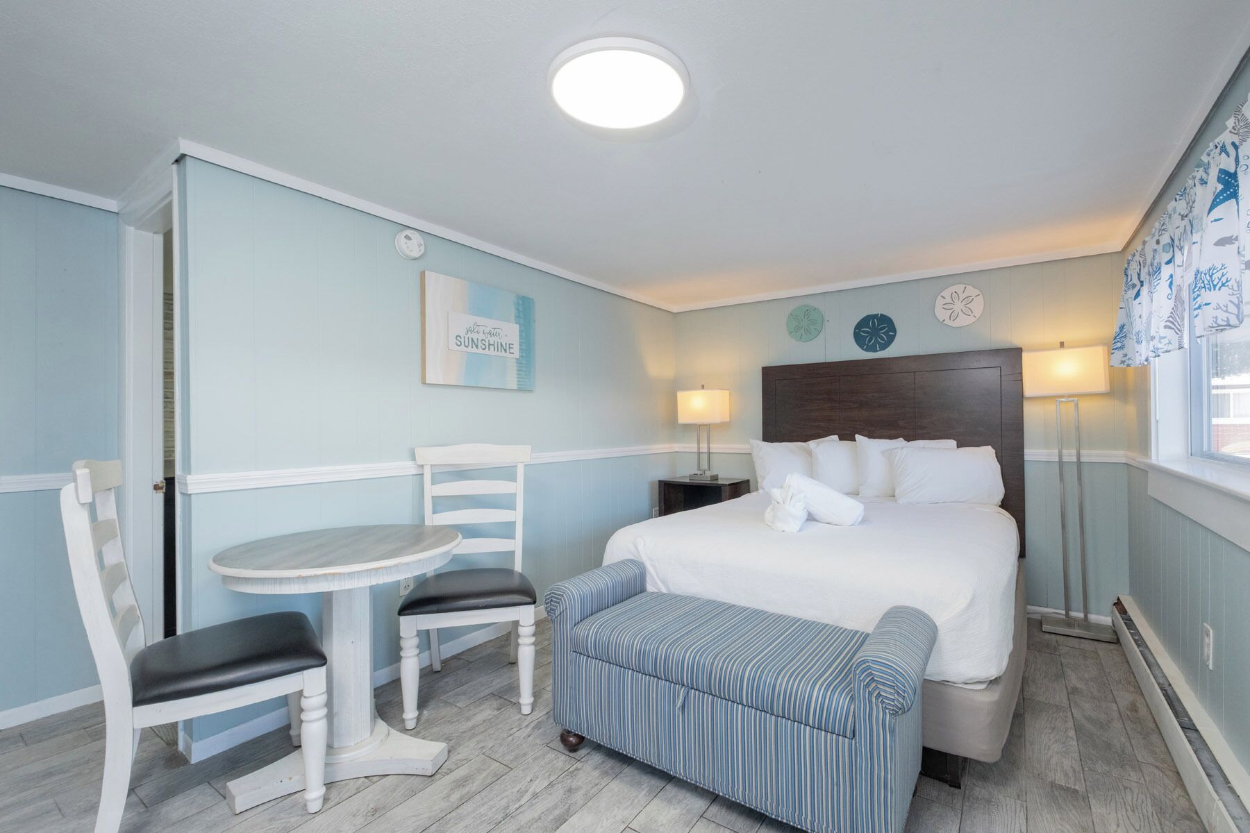 Une chambre à coucher comprenant un lit, des tables de chevet, une chaise, une petite table et un banc.