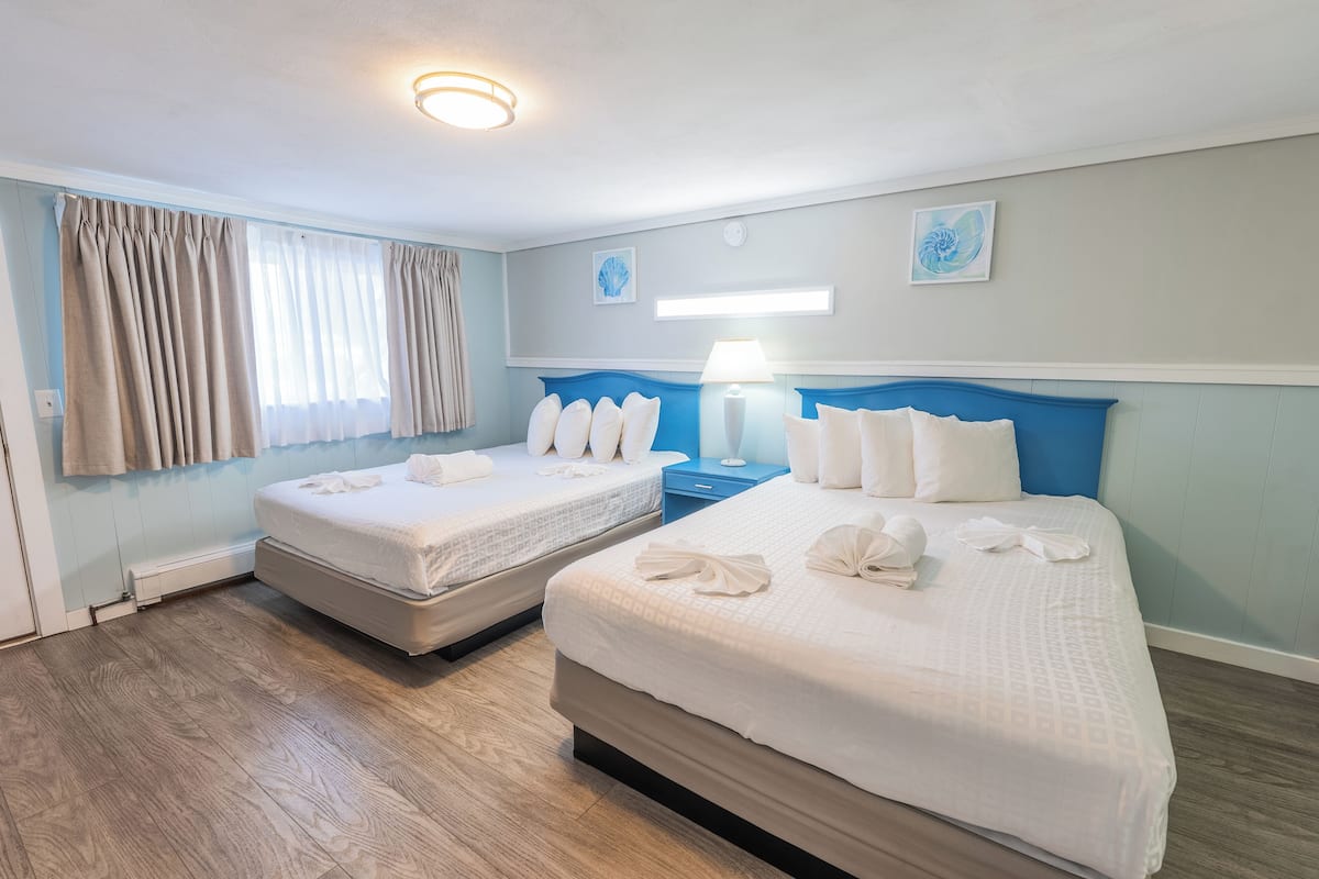 A hotel room with two beds, a nightstand, a lamp, and artwork on the walls.