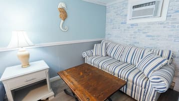 A room with a striped sofa, a wooden coffee table, a white nightstand with a lamp, and a brick-patterned wall.