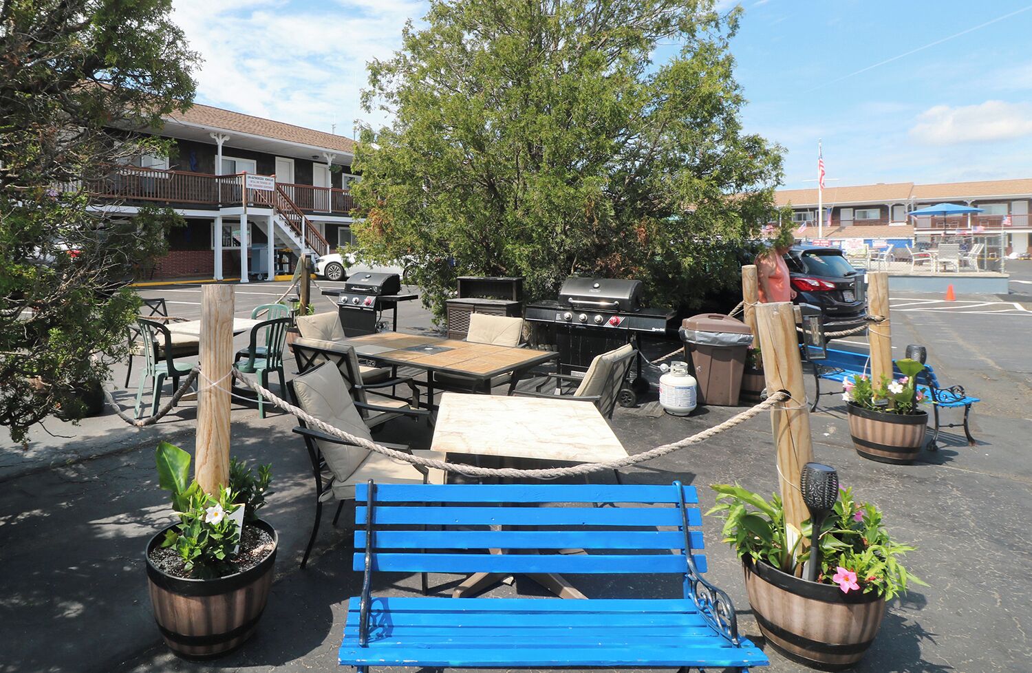An outdoor seating area with a blue bench, tables, and chairs, surrounded by potted plants.