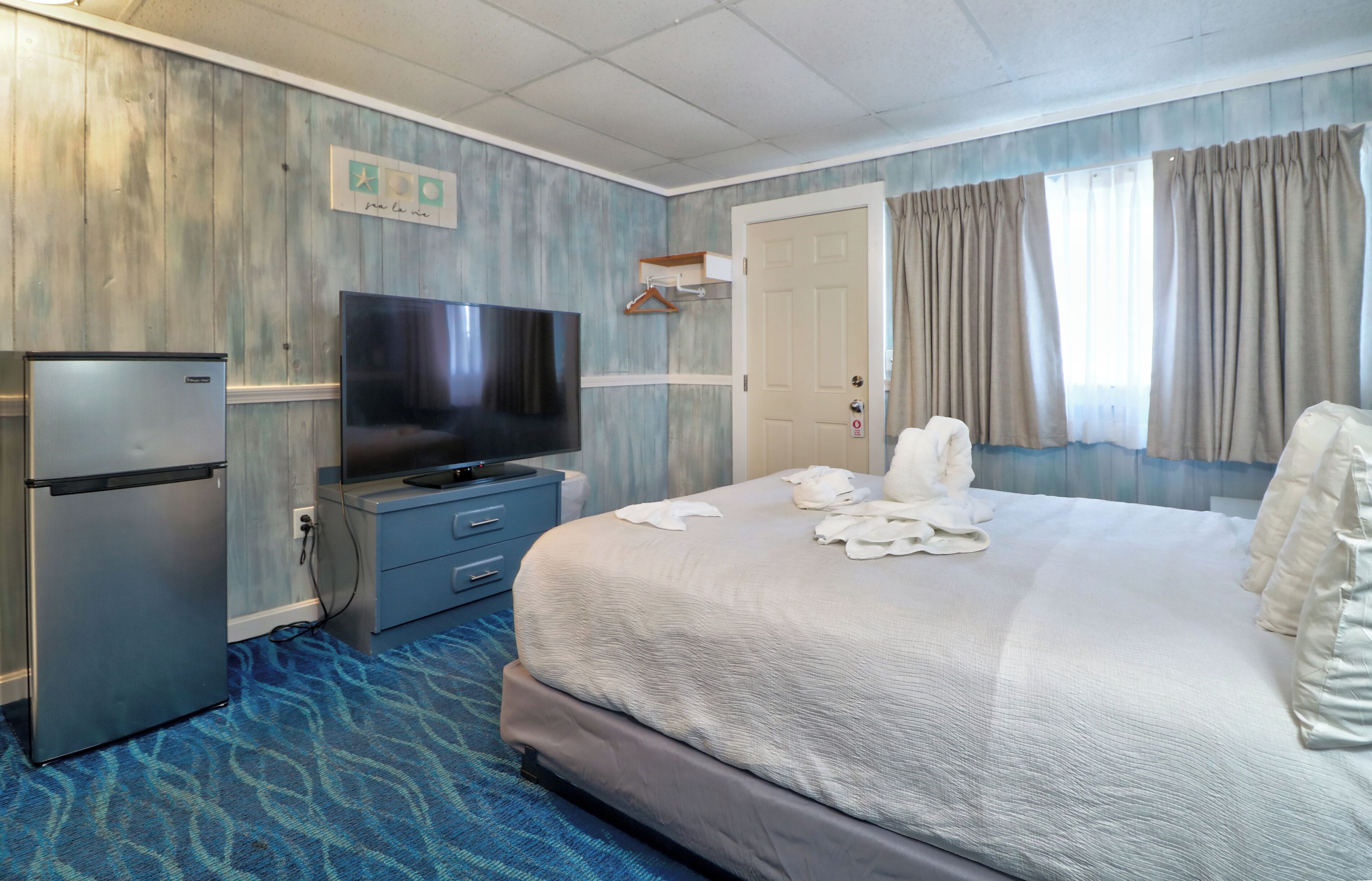 Habitación de hotel con cama, televisión, refrigerador y puerta al baño.